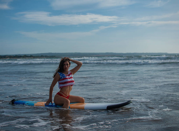 Beach lifestyle people - woman enjoying summer sun and blue sky sitting relaxing with surfboard after bodyboarding in water. Beautiful multiracial Asian Caucasian female bikini girl on travel vacation - Photo, image
