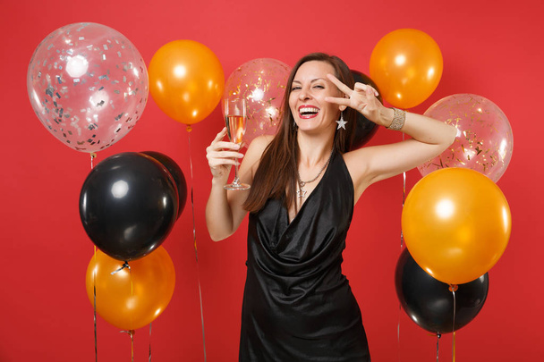 Chica riendo en vestido negro celebrando la celebración de la celebración de la copa de champán, mostrando signo de victoria en los globos de aire de fondo rojo brillante. Día de San Valentín, Feliz Año Nuevo, concepto de fiesta de cumpleaños mockup
 - Foto, Imagen