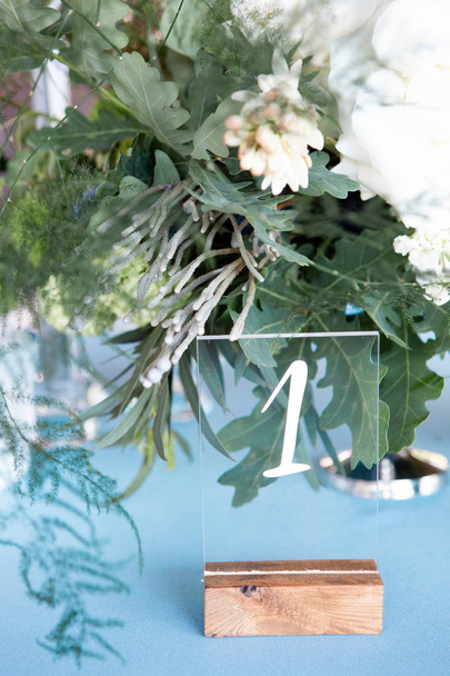 Espace décoré avec petite plaque de verre de numéro de table, fleurs et verts sur le fond
 - Photo, image