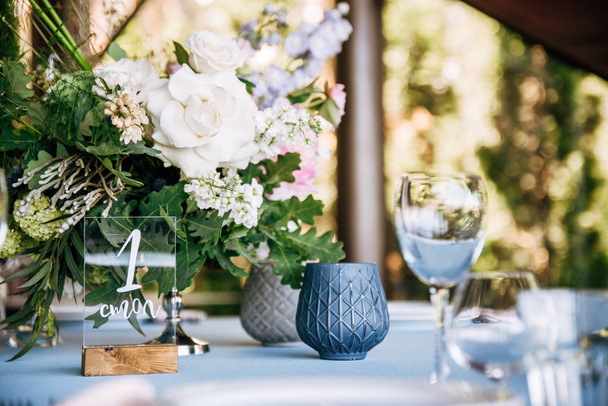 Святковий круглий стіл з синьою скатертиною, посудом, келихами для вина та букетом квітів у центрі
 - Фото, зображення