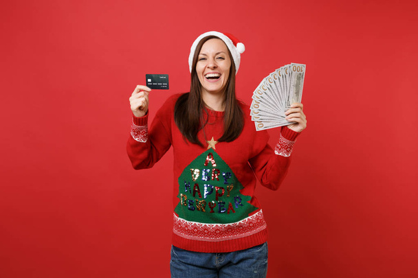 クレジット カードを持っているサンタ少女は笑って、たくさんのドル紙幣、明るい赤の背景に分離された現金お金の束。幸せな新しい年 2019年お祝いの休日党の概念。コピー スペースをモックアップします。 - 写真・画像