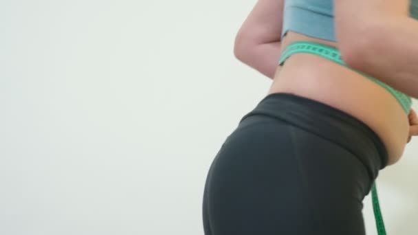 The concept of overweight and weight loss. A woman measures herself with a measuring tape in the bedroom. Looking at herself in the mirror - Footage, Video