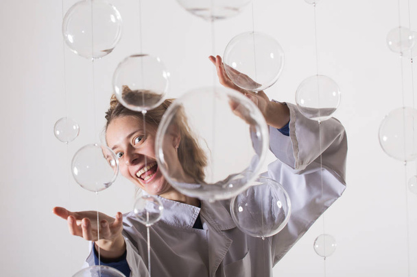 A mad scientist is experimenting with glass balls. A woman in a white robe smiles strangely and stretches her arms forward. The blonde is trying to hug someone. Photo for fans of physics and chemistry. Glass balls in the foreground, behind white back - Valokuva, kuva