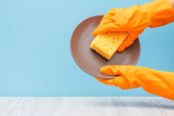 Naisten kädet oranssi suojakäsine lautasella ja sienellä sinisellä pohjalla. Pesu ja puhdistus käsite
. - Valokuva, kuva