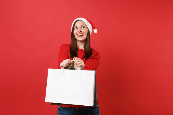 Dreamy young Santa girl looking up, holding packages bags with purchases after shopping isolated on bright red background. Happy New Year 2019 celebration holiday party concept. Mock up copy space - Photo, image