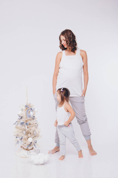 pregnant woman and little girl dress up Christmas tree with white balls on white background - Fotoğraf, Görsel