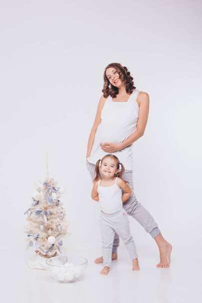 pregnant woman and little girl dress up Christmas tree with white balls on white background - Foto, afbeelding