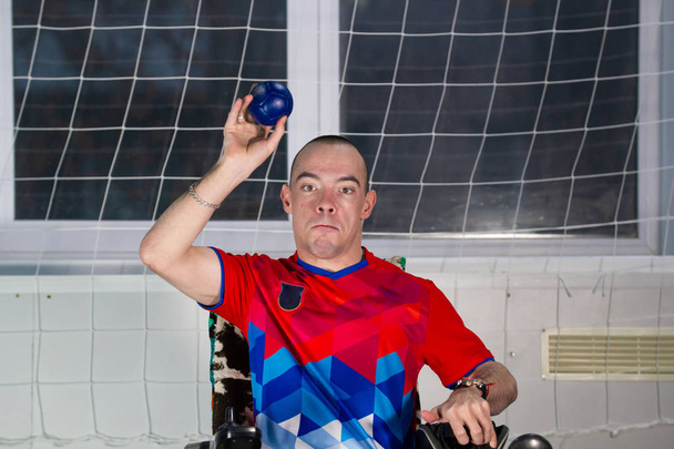 Бочча. Инвалид-спортсмен, сидящий в инвалидном кресле и размахивающий маленьким голубым мячиком
 - Фото, изображение