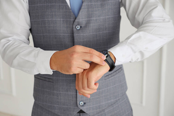 Succesvolle man in een vest raakt zijn horloge - Foto, afbeelding