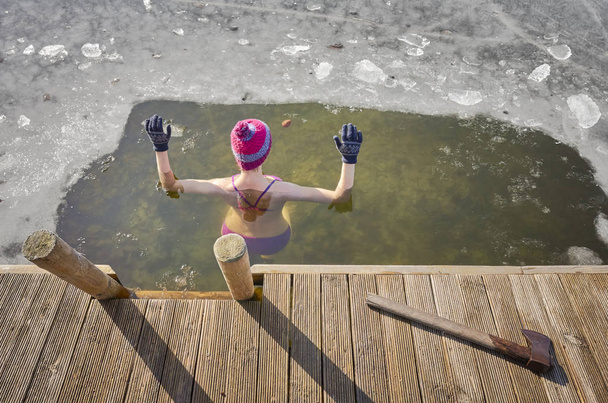 Mujer en forma realiza baño de hielo en el agujero de hielo. Tomar las manos por encima del agua protege de la hipotermia rápida
. - Foto, Imagen