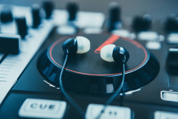 In ear headphones lying on DJ midi controller platter. Focus on earpods. Start the party now  - Foto, Imagem