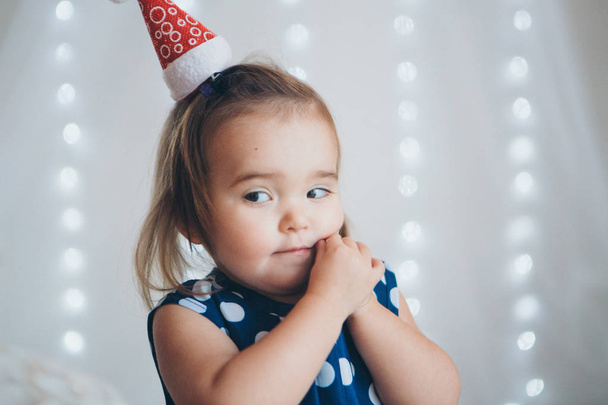portrait of a little girl in a red Christmas cap on the background of lights - Fotoğraf, Görsel