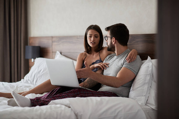 Young man and woman working on laptop in bed - Φωτογραφία, εικόνα