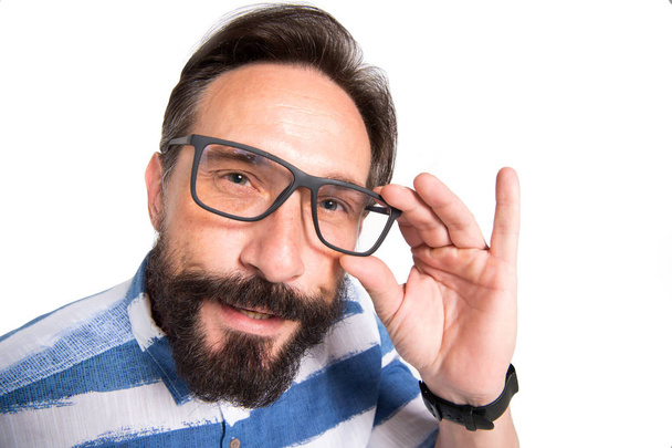 Interrogative glance of smart mature man looking at you while touching the rim of his glasses and keeping his mouth slightly open - Foto, immagini