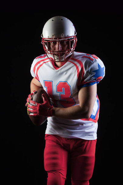 American football player wearing helmet ready to throw ball on black background - Photo, Image