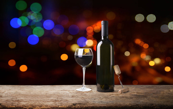 red wine glass near bottle with light bokeh in background - Foto, Imagen