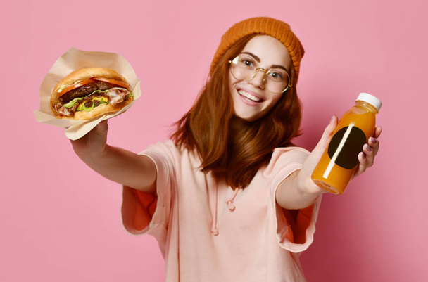 Piękne nastoletnie dziewczyny z rude włosy i kapelusz gospodarstwa burger i napojów w obie ręce. - Zdjęcie, obraz