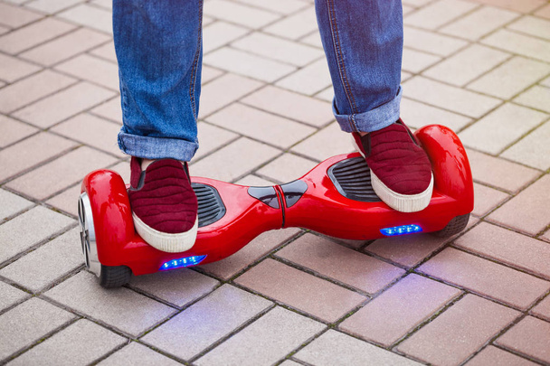 Feet of a girl riding on modern red electric mini segway or hover board scooter. Trending new transportation technology that is so much fun and easy to ride and produces no air pollution to the atmosphere. Close up on model legs and gadget. - Foto, immagini