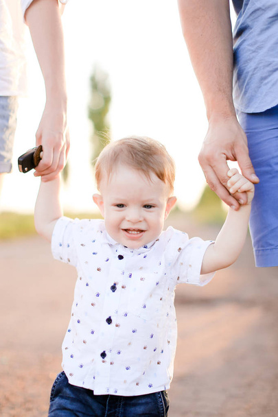 Usmívající se dítě drží za ruce rodiče a chůze po silnici. - Fotografie, Obrázek