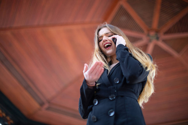 Hermosa joven hembra en traje elegante gritando y haciendo gestos mientras es despedida del trabajo por teléfono en el parque
 - Foto, Imagen
