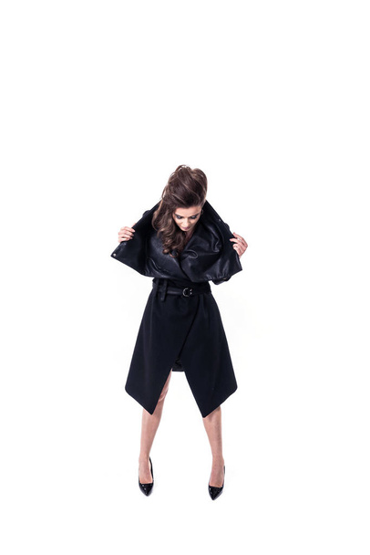 young woman in designed black coat with leather details and big trendy collar posing on white background - 写真・画像