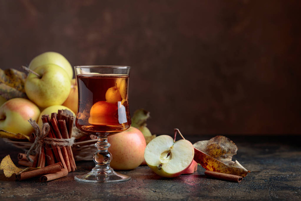 Glas appelsap of -cider met sappige appels en kaneelstokjes op een keukentafel. - Foto, afbeelding