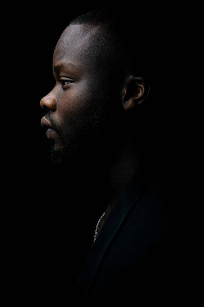Dark key portrait of young man in profile, weared in black jacket. Studio shot. - Фото, изображение