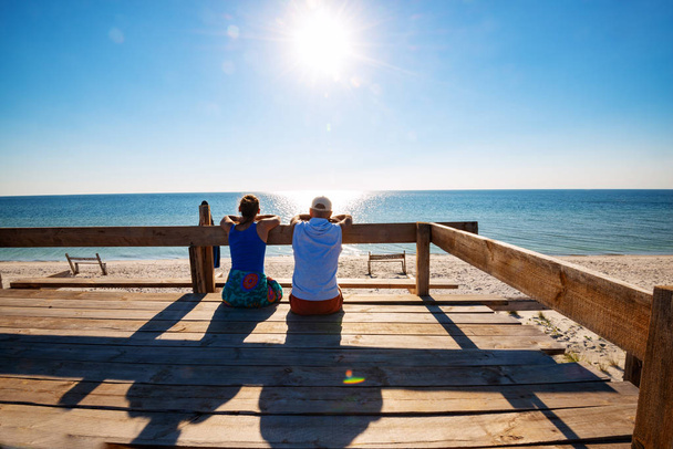 glückliches Paar entspannt sich auf einer Bungalow-Veranda, bewundert das türkisfarbene Meer und genießt das Leben an sonnigen Tagen. erstaunliche Reise an die Küste. Rückseite, hinterleuchtet. - Foto, Bild