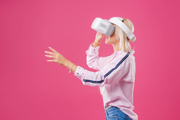 Young Blond happy woman student with virtual reality goggles. Studio shot on pink background. Virtual learning - Фото, изображение
