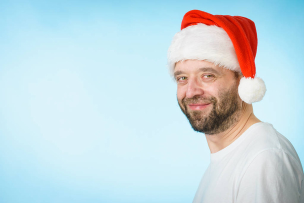 Bearded man wearing santa claus hat portrait, on blue with copy space. Christmes time. - Fotó, kép