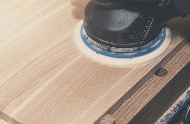 Rectificadora eléctrica manual con rueda de esmeril muele la caja de madera, tablero. carpintería, taller. Fabricación de productos de madera
 - Foto, imagen