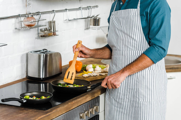 cropped image of mature man cooking vegetables on frying pan in kitchen - Foto, Imagen