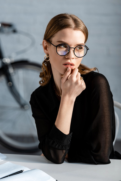 attractive businesswoman in black clothes sitting on chair and touching chin - Photo, Image