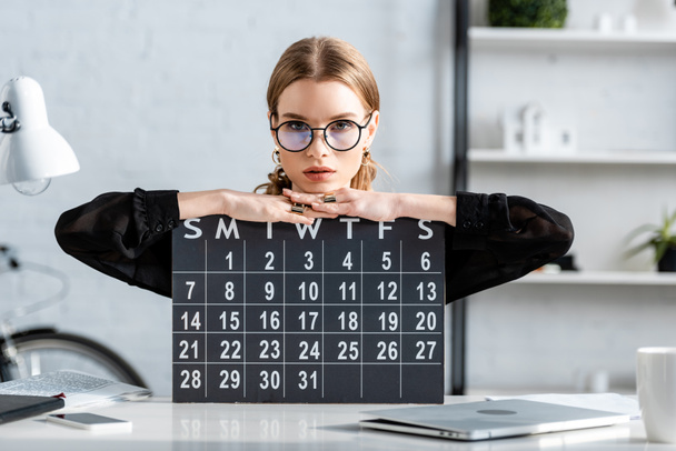 όμορφη επιχειρηματίας με μαύρα ρούχα και τα γυαλιά, κάθεται σε καρέκλα και κρατώντας ένα ημερολόγιο - Φωτογραφία, εικόνα