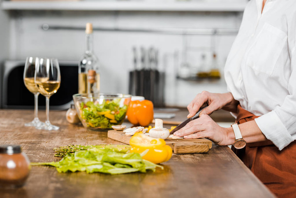 обрезанный образ зрелой женщины, режущей овощи на деревянной доске на кухне
 - Фото, изображение