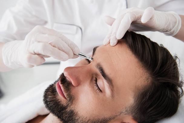 Calm bearded man undergoing plucking eyebrows procedure - Фото, изображение