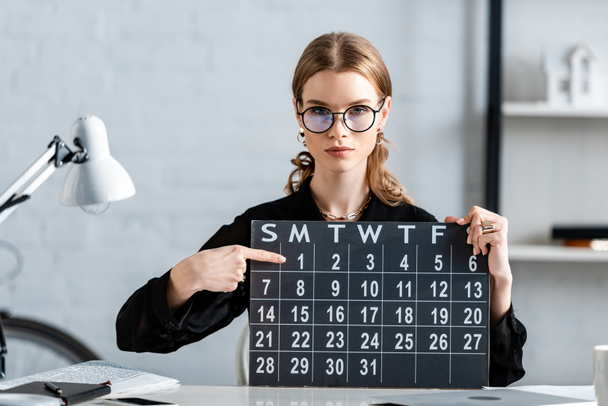 atrakcyjna kobieta interesu w czarne ubrania i okulary gospodarstwa kalendarza i datą - Zdjęcie, obraz