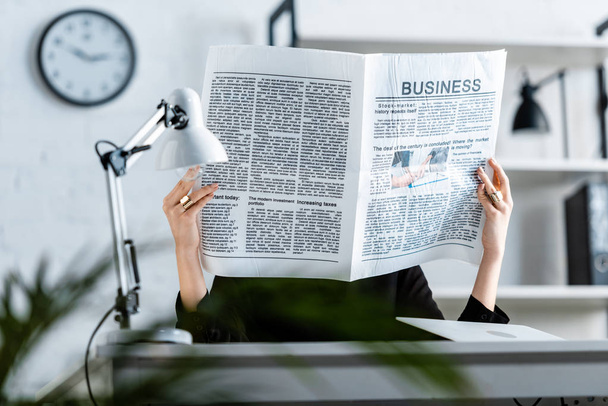 empresária em roupas pretas sentado na cadeira enquanto segurando jornal de negócios na frente da cara
 - Foto, Imagem