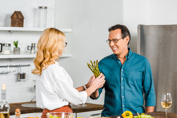 dojrzały mąż dając szparagi do żony, do gotowania w kuchni - Zdjęcie, obraz