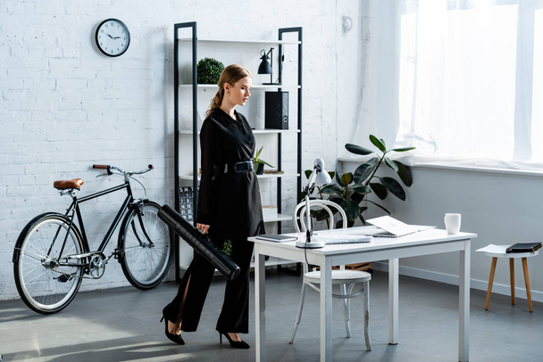 mooie zakenvrouw in zwarte kleding permanent op kantoor en kijken naar laptop - Foto, afbeelding