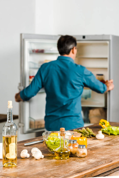 Achteraanzicht van de volwassen mens op zoek naar een koelkast in keuken - Foto, afbeelding
