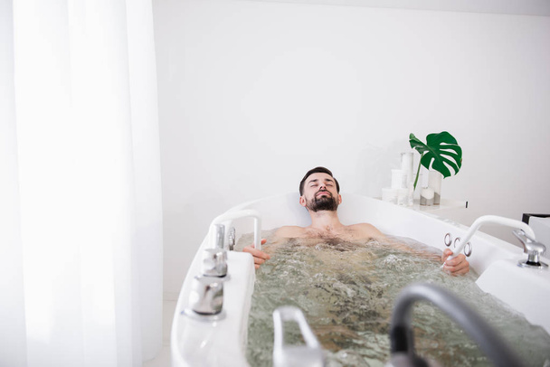 Peaceful bearded man enjoying sitting in hydro massage bathtub - Foto, Imagen
