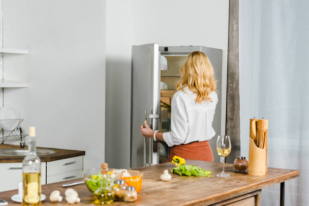rear view of mature woman taking something from fridge in kitchen - Foto, Imagem