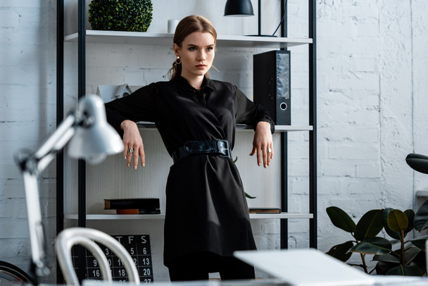 selective focus of serious woman in black formal wear at workplace - Foto, afbeelding