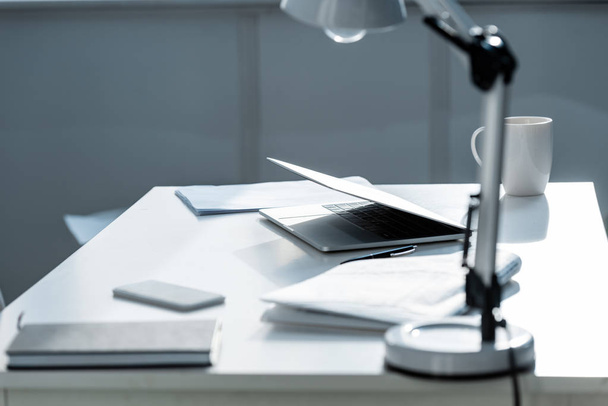 table blanche avec lampe, documents, carnet et ordinateur portable
 - Photo, image