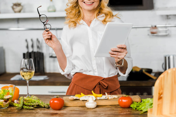 cropped image of smiling mature woman using tablet in kitchen - Zdjęcie, obraz
