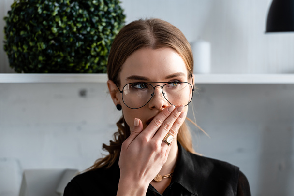 portrait of beautiful woman in glasses covering mouth with hand and looking away - Photo, Image
