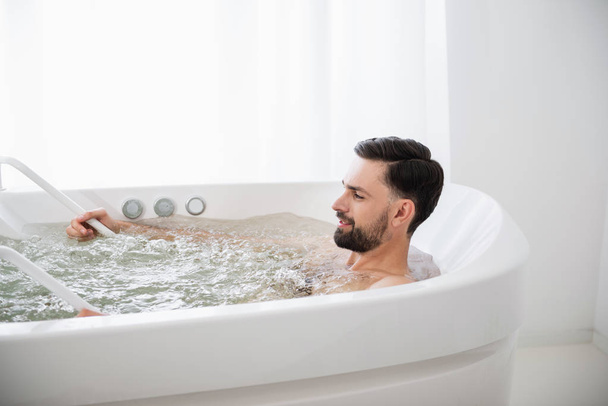 Close up of curious man trying hydro massage and looking glad - Φωτογραφία, εικόνα