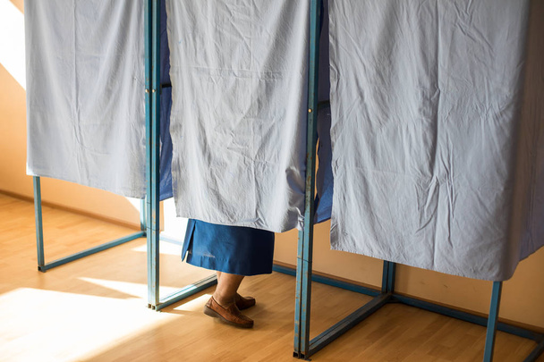 Farbbild einer nicht identifizierbaren Person, die während der Wahlen in Wahlkabinen in einem Wahllokal ihre Stimme abgibt. - Foto, Bild