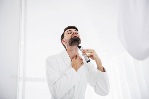Man in white bathrobe putting head up while shaving his neck - Photo, image